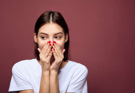 A sad, scared girl found out the bad news and covered her mouth with her hands, looking to the side. Beautiful young woman in a white T-shirt posing on a pink background standing straight.Copy space.の写真素材