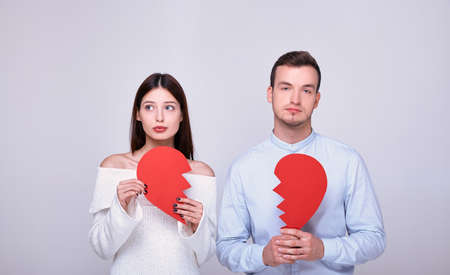 A couple of lovers with a broken heart. Girl with blue eyes in a white knitted sweater stands next to a young guy in a shirt with half a heart. The concept of Valentine's Day and broken love.の写真素材