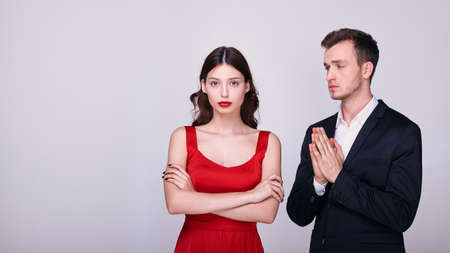 Caucasian young woman in a red dress with bright makeup crossed her arms over her chest and looks straight. Quarrel and forgiveness of a young couple. Copy space.の写真素材