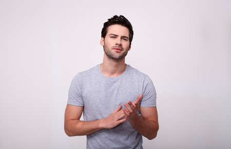 Handsome young man in a gray t-shirt looking at camera, standing on gray background.の写真素材