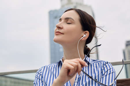 A charming business lady sits in the park on a brown bench and breathes the air of freedom and changes for the better. Lunch break, rest, worker.の写真素材