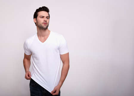 Gorgeous charming handsome sports man with a chic sports figure, with dark volsos and a beard, in a white T-shirt goes forward. Sexy brunette poses in the studio on a white background. Copy space.の写真素材