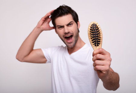 A screaming man screams in fear, holds a comb and touches his chic black hair. Men's problem of hair...