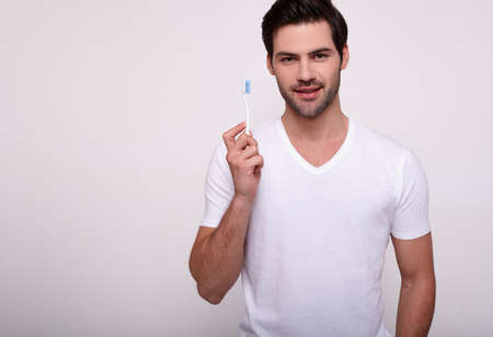 A handsome young man in a white T-shirt is going to brush his teeth, engaged in morning routine, oral hygiene. The concept of health, healthy teeth, dentistry, bleeding gums. Copy space.の写真素材