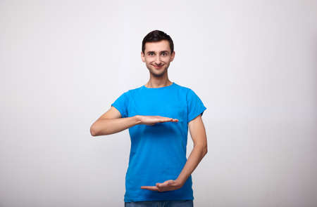 A man in a blue T-shirt shows his hands the distance or size of some object. Guy, smiling and holding out his hands to his side, like he's sizing up something but with empty space between the hands.の写真素材