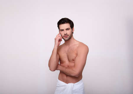 A cute, engaging young, shirtless white man poses in the studio on a white, grey background. The concept of male strength and beauty. Copy space.の写真素材