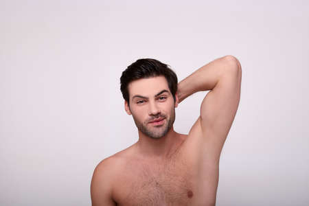 Cool brutal brunette man smiles cutely and holds his hand behind his head. The eyes are wide open, the guy is surprised. Beauty concept. Copy space.の写真素材