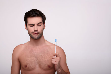 A surprised, handsome, muscular white man with dark hair and a perfect body holds a toothbrush in...