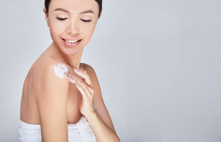 Woman with natural make-up and portrait of healthy skin. Beautiful asian girl model touching fresh glowing moisturized facial skin on light background closeup. Skin care concept. Copy space.の写真素材