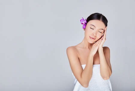 Closeup, copy space. Beauty concept, body care. Pretty asian girl with closed eyes and folded arms under the cheek. Behind the ear of a beautiful delicate purple flower. Copy space.の写真素材