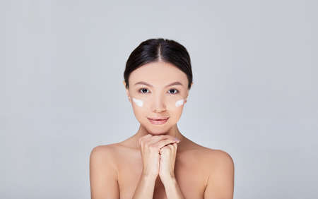 Laughing girl applying moisturizing cream on her face. Photo of young girl with flawless skin. Skin care and beauty concept. Copy space.の写真素材
