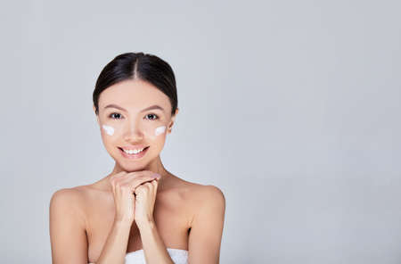 Youthful smiling pretty Asian woman with hand touching face on white background for beauty and skin care concepts. Skin care concept. Copy space.の写真素材
