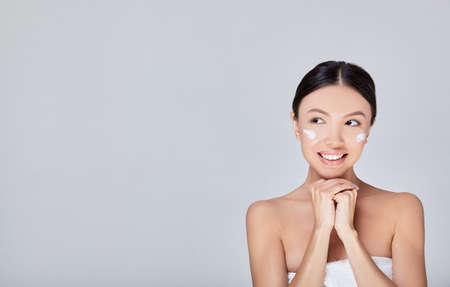 Attractive tender beautiful young Asian woman with clean and fresh skin and healthy hair, in a white towel smiles and looks to the side. Spa treatments. Strong hair and a healthy body. Copy space.の写真素材