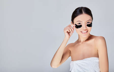 A close up, young woman uses patches under the eyes in a studio smile make-up skin care portrait clean beautiful cosmetic health beauty care portrait perfect. Copy space.の写真素材