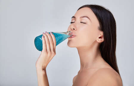 Beautiful young lady drinking fresh vitamin cocktail. The concept of a healthy lifestyle, organic detox juice with nutrition of exositical fruits. Vegan food, raw food diet. Health and beauty.の写真素材