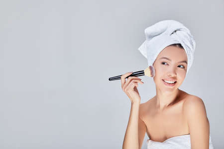 Beautiful Asian woman in a white bath towel on her hair and body wokurg, with a cosmetic brush for makeup. A young girl came out of the shower and makes a make-up. Copy space.の写真素材