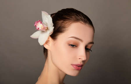 Beauty portrait of an attractive sensual brunette topless woman standing isolated over brown background, posing with orchid flower, look down.の写真素材