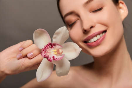 People, dehydration, skin care and beauty concept. Beautiful girl with orchid flowers. Beauty Model Woman Face. Perfect skin. Professional makeup. Beautiful woman face close up portrait hands on skin.の写真素材