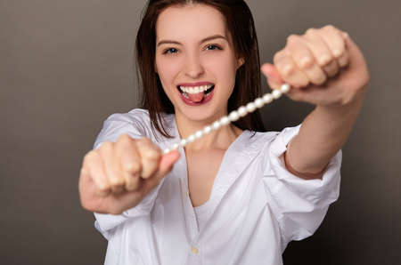 Lovely cheerful girl with dark wet hair and blue eyes, in a white shirt, holds pearl beads in her hands, laughs, expresses emotions, skin care concepts, portrait. Natural cosmetics, pearl extract.の写真素材