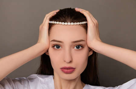 Gorgeous girl with dark wet hair, blue eyes, beautiful healthy skin, in a white shirt, with pearl on the hair, spa concept, close up portrait, holding a product. Natural cosmetics, pearl extract.の写真素材