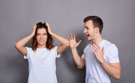 Couple of young woman and man in white basic t-shirts and feuds standing isolated over gray background. The concept of a crisis of relations, family problems, domestic violence.の写真素材