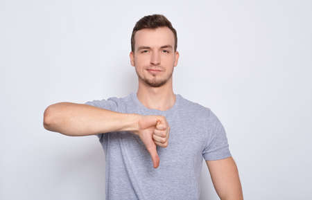 Young pretty man with green eyes and blond hair shows thumb down rating for something negative, isolated on white background.の写真素材
