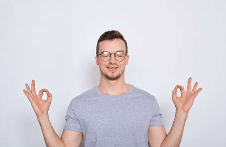 Concentrated nice calm man in a gray T-shirt standing with his eyes closed, relaxing during meditation, trying to find balance and harmony. Yoga and meditation concept.の写真素材