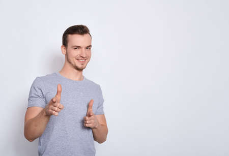 A young man in a gray T-shirt is smiling, showing a thumbs up with positive emotions and happiness, isolated on a white background. Satisfaction with quality and recommendation. Copy space.の写真素材