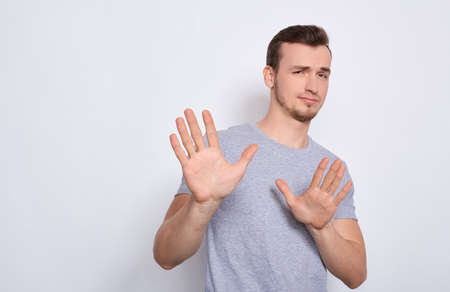 A young handsome white guy in a gray basic T-shirt, stretched his arms forward, shows his hands stop, does not want. The sad man says timeout, stop, shows reluctance.の写真素材