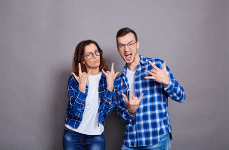 Excited beautiful couple wearing white t-shirts, blue plaid shirts, glasses, standing isolated on gray background, showing thumbs up, dancing, wild fun, having fun.の写真素材