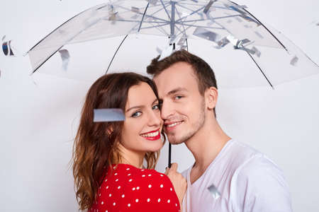 Portert, beautiful young happy couple in love together, laughing, couple hiding under an umbrella from falling confetti, cuddling, looking straight isolated on white background.の写真素材