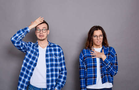Amazed sad woman and man shrug hands, have no idea, are dressed in casual clothes, posing on a gray background. Confused into question a couple with an ignorant expression in the room.の写真素材