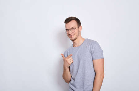 Young smiling man in a gray basic t-shirt with round glasses for vision, looking at the camera, copy space for advertising isolated on a white background. Copy space.の写真素材