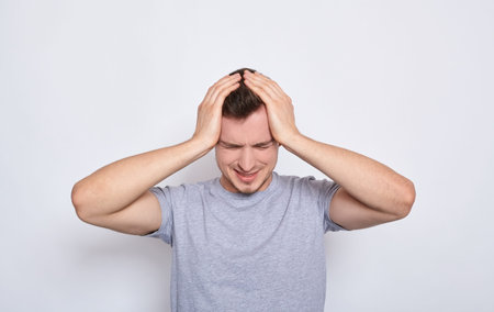 Young caucasian man isolated on a white background in a gray casual t-shirt touching his temples...