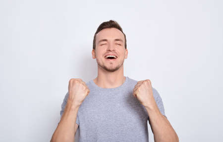 Soccer fan isolated. A young attractive man in a gray basic t-shirt shouted while his team won, raised both fists in a victory gesture. Copy space.の写真素材