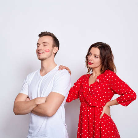 Close up, young white couple in love, he, she, together forever, the girl stands behind the guy, joyful and cheerful, a girl in red and a guy with a kiss on the cheek.の写真素材