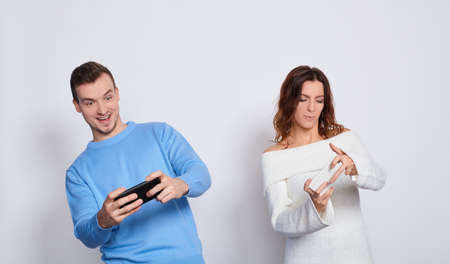 Young caucasian cute cheerful couple two friend boyfriend girl isolated on a white background. People lifestyle concept. Layout copy space. Playing video games with mobile phonesの写真素材