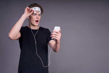 A shocked surprised young guy with a phone in his hand, looks like he cant go to the rally, make a message about the refusal. People, emotions and technology concept. Copy space.の写真素材