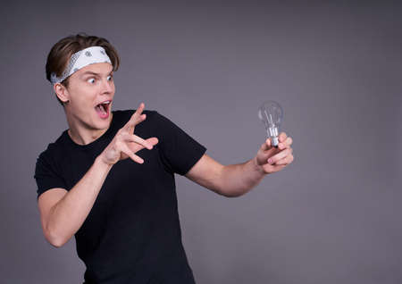 Hurrah! Portrait of excited cheerful glad, delightful handsome shocked astonished surprised man in black t-shirt with light bulb isolated on gray background. Copy space.の写真素材