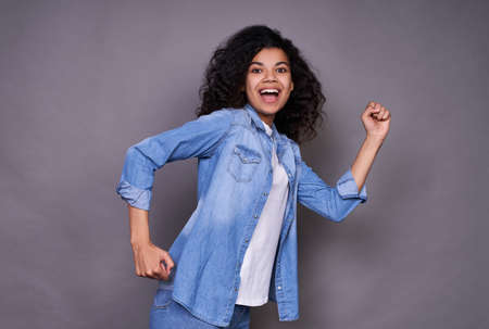 Portrait of a cheerful young African-American girl, a joyful thousand-year-old African-American girl walks through the air, runs to the right against a gray studio background, smiles at the camera.の写真素材