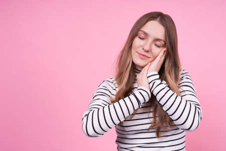 A young, cute, graceful Caucasian blonde, gently and satisfiedly presses her hands to her face, eyes closed, wants to relax, enjoy, in harmony.Copy space.の写真素材