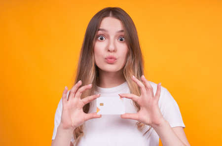 Young cute funny caucasian girl holding a credit card in hands, over isolated yellow background,の写真素材
