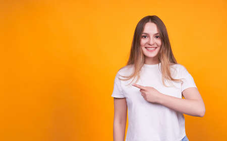 Young cute and pretty girl in a white T-shirt on a yellow isolated background, smiling, pointing her finger to the left to space for your advertisement or text.の写真素材