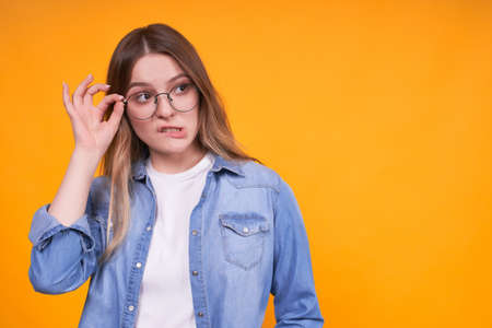 Cute charming caucasian girl with a funny confused face in a denim jacket holds glasses and looks to the right.Copy space.の写真素材