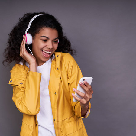 Charming happy young African American girl in white T-shirt and a yellow raincoat, with curly hair,...