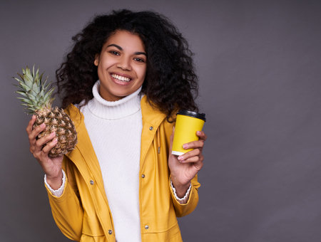 Close-up portrait of a charming dark-skinned young woman with curly hair, in a white sweater and...