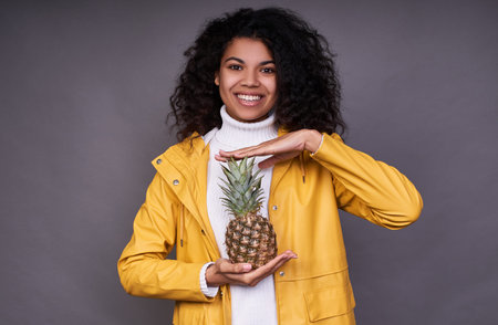 Gorgeous charming dark-skinned young woman with curly hair, in a white sweater and a yellow jacket,...