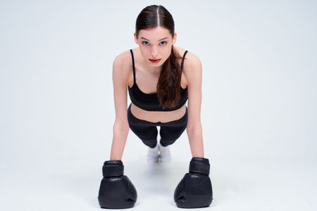 Charming cute young fresh Caucasian girl in a black sports suit for sports, sitting on a white...
