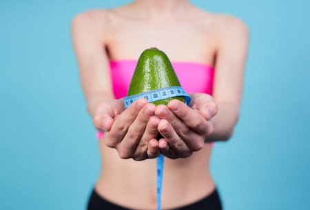 Cropped frame, a young white girl, in a pink top, holds an avocado in her hands, wrapped in a blue...
