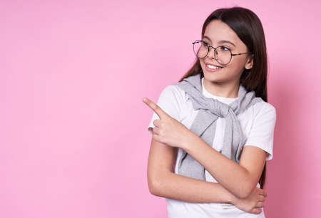 Young cute Caucasian brunette schoolgirl with glasses, smiling, holds a book in her right hand in her left hand, concept of planning ideas, a prolific decision, brilliant answer on a pink background.の写真素材